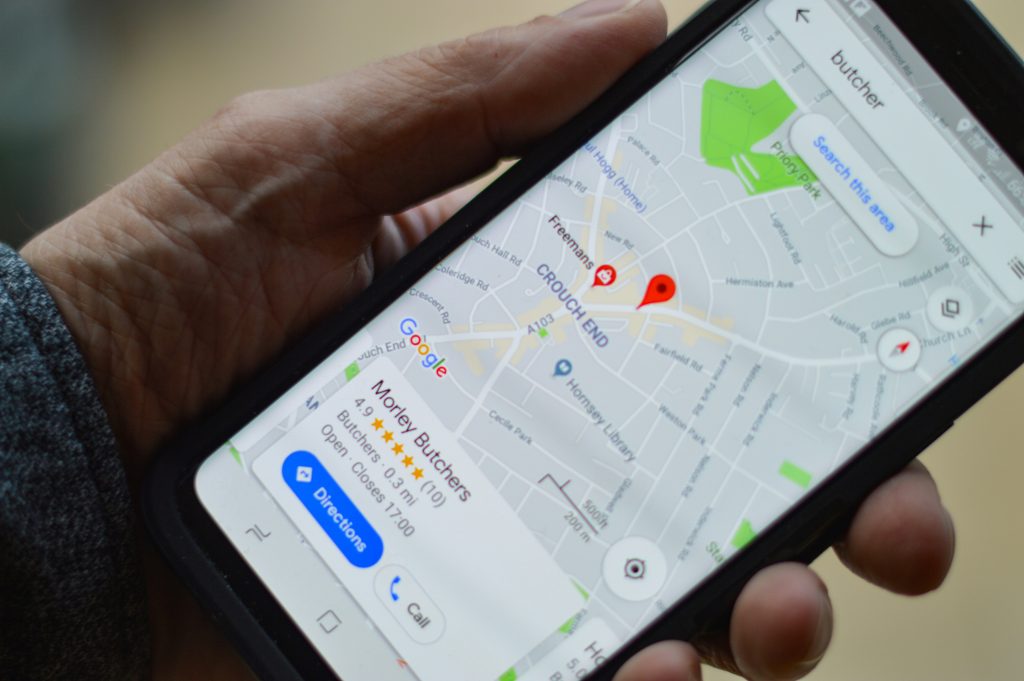 Local Marketing Google My Business Lokales Marketing: Eine Hand hält ein Smartphone in der Hand. Darauf ist ein Maps-Eintrag von einem Google My Business Profil zu sehen.